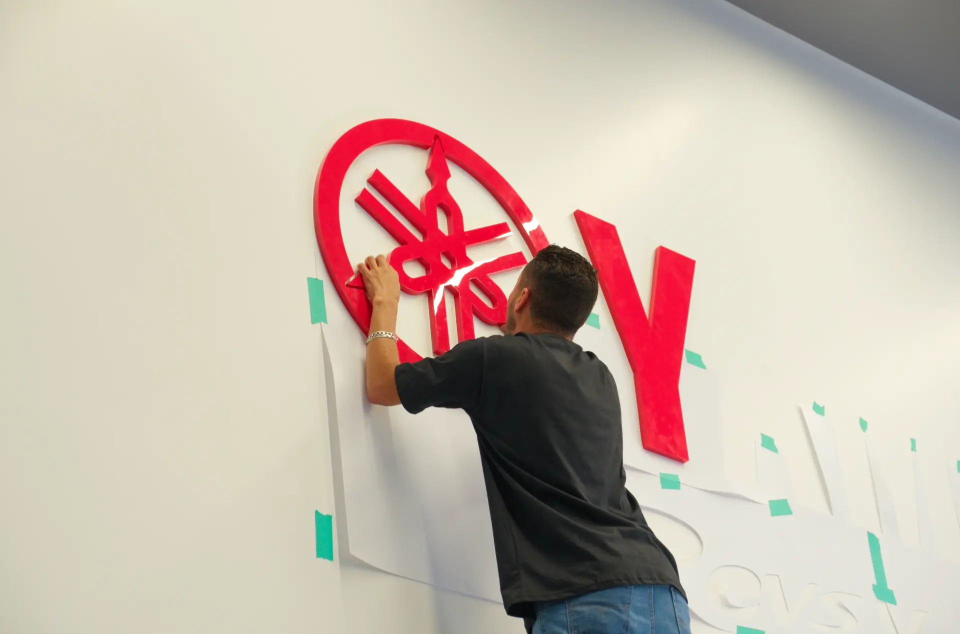Instalador posicionando o logo circular Yamaha vermelho no paredão branco da loja